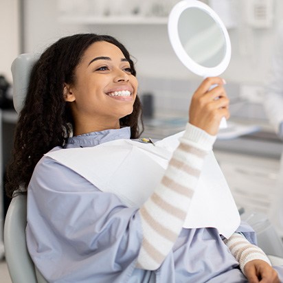 Woman smiling at reflection in handheld mirror