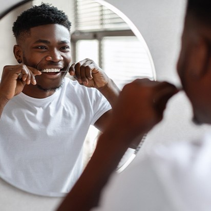 Patient smiling while flossing his teeth in bathroom