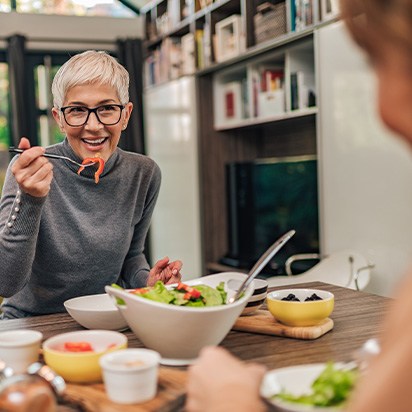 Woman smiling while eating lunch with friend in kitchen