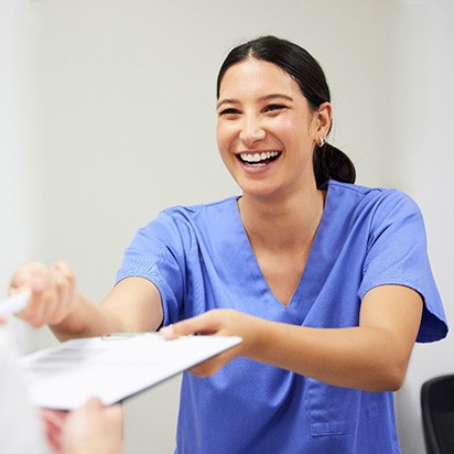 Smiling dental assistant handing patient forms
