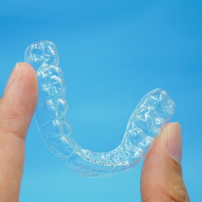 Two fingers holding Invisalign aligner against blue background