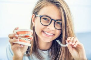 Young girl holding Invisalign trays and model of traditional braces