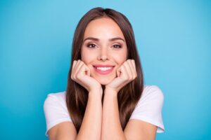 Woman smiling with straight, white teeth, holding fists to her face in happiness.
